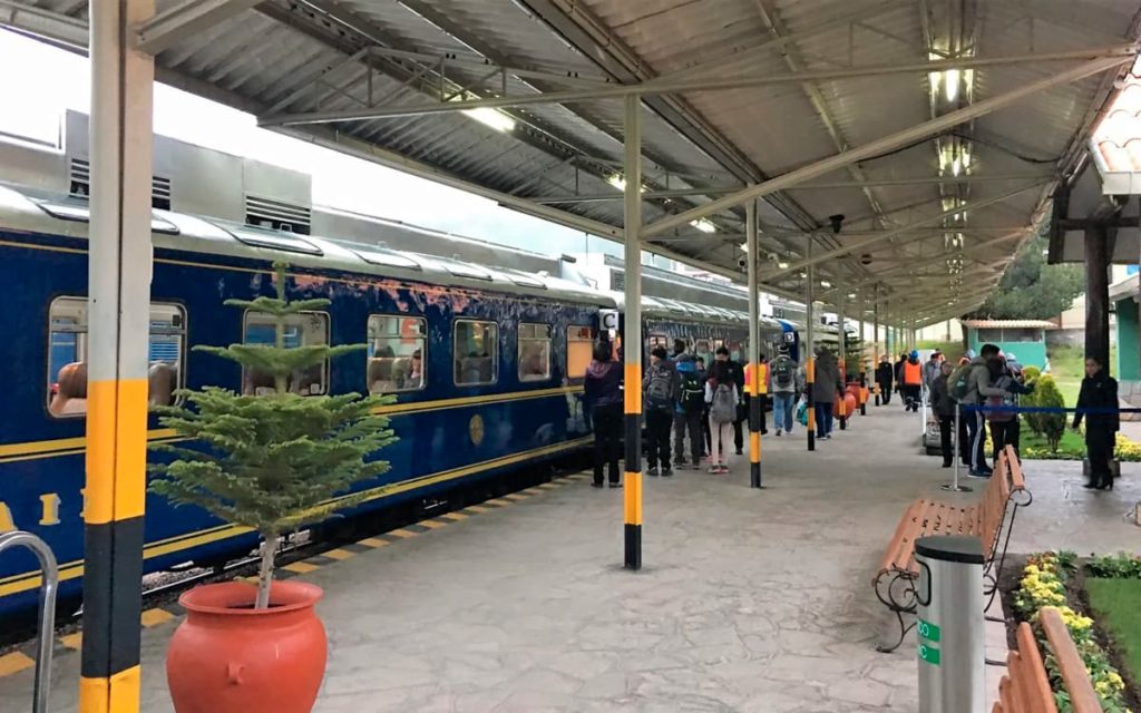 Andén de la estación de tren de Ollantaytambo con un tren azul de PeruRail