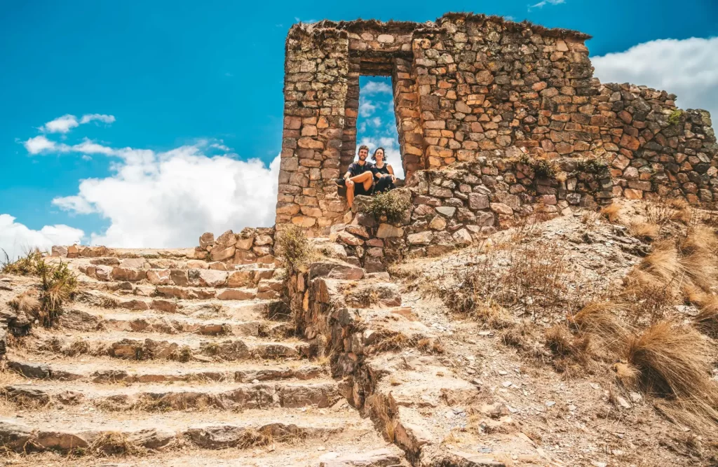 Senderistas disfrutando de la vista desde Cachicata Inti Punku, con terrazas incas y montañas distantes bajo el sol.