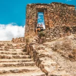 Senderistas disfrutando de la vista desde Cachicata Inti Punku, con terrazas incas y montañas distantes bajo el sol.