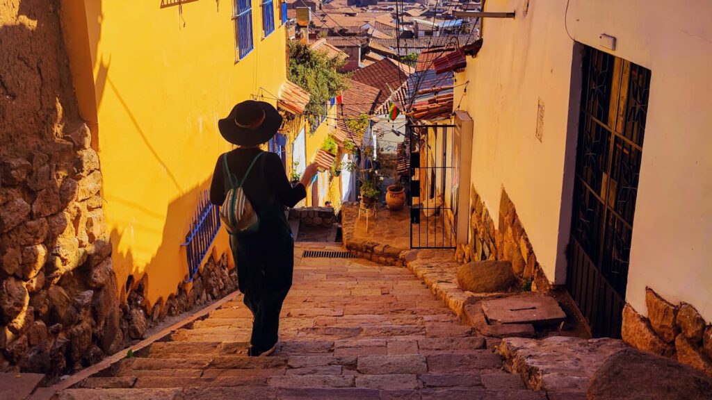 Viajera bajando una calle empedrada con escalinatas en el barrio de San Blas, entre casas coloniales de muros amarillos