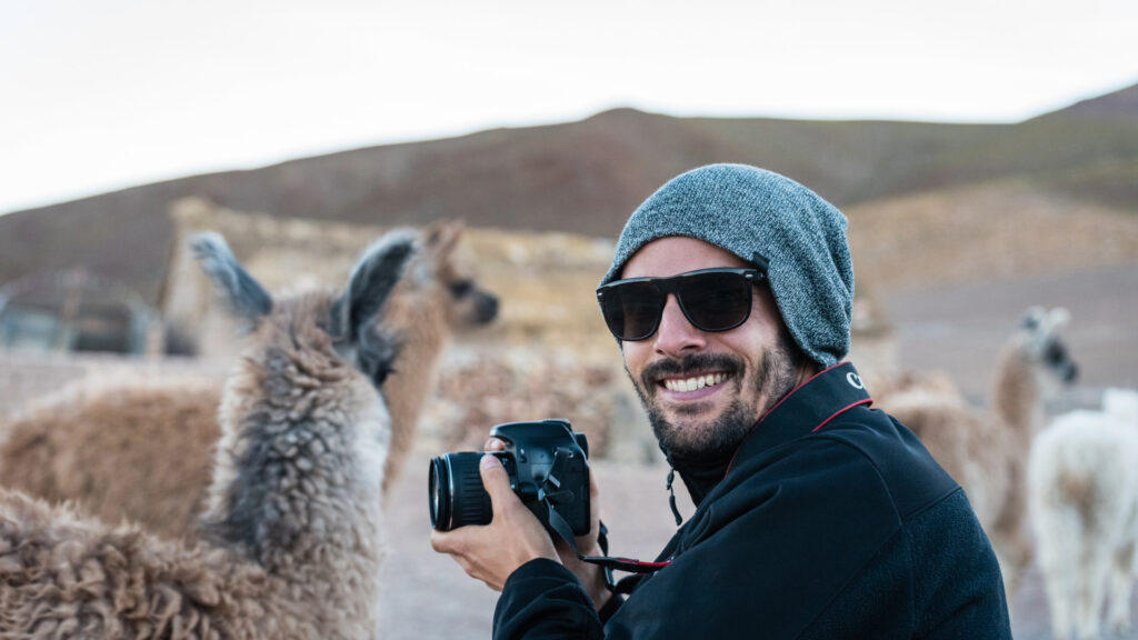 Viajera sonriente fotografiando llamas en un paisaje andino