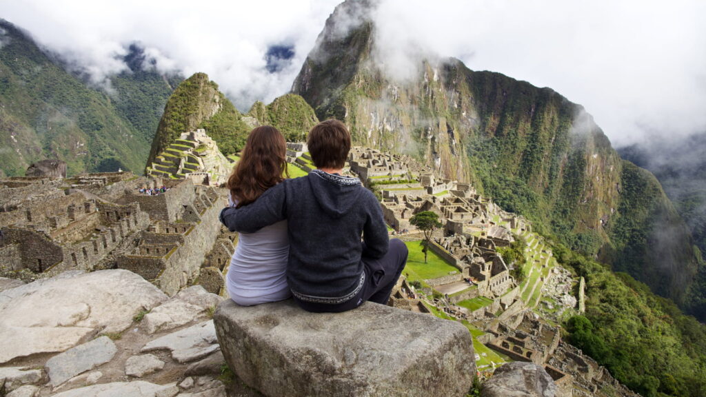 Pareja sentada en un mirador frente a la ciudadela de Machu Picchu contemplando sus terrazas y templos