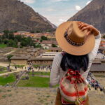 Mujer con sombrero observando las ruinas y el pueblo de Ollantaytambo en el Valle Sagrado - Cusco tu Destino Travel