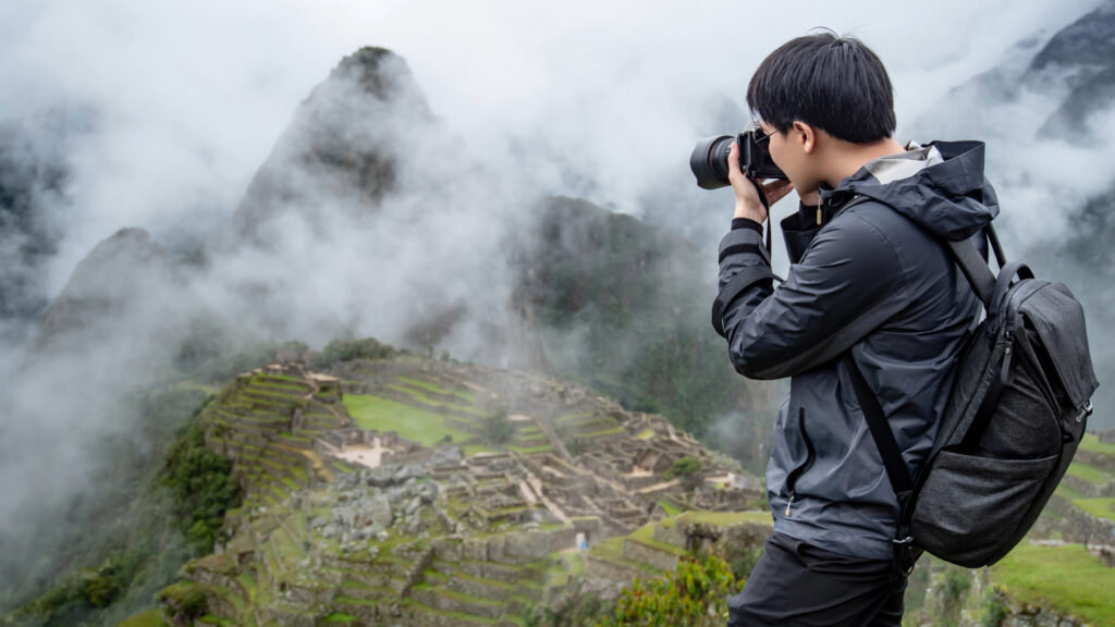 Viajero fotografiando la ciudadela de Machu Picchu envuelta en neblina desde la parte alta