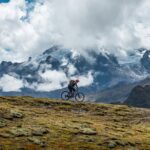 Ciclista de montaña recorriendo un sendero en lo alto de los Andes, con el imponente glaciar del Apu Veronica cubierto de nubes al fondo.