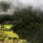 La plaza principal y las ruinas de Choquequirao emergiendo de una densa niebla matutina sobre la verde montaña de los Andes peruanos.