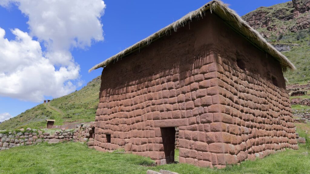 Antigua construcción inca de piedra con techo de paja y puerta trapezoidal en el complejo arqueológico de Huchuy Qosqo, Perú.