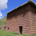 Antigua construcción inca de piedra con techo de paja y puerta trapezoidal en el complejo arqueológico de Huchuy Qosqo, Perú.
