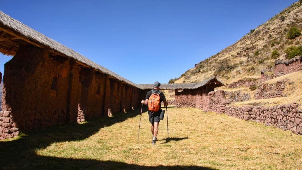 Excursionista con mochila caminando entre los imponentes muros de piedra y adobe del sitio arqueológico inca de Huchuy Qosqo, Perú.