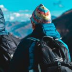 Dos excursionistas de espaldas, equipados con mochilas y gorros, hacen una pausa para admirar el vasto paisaje de montañas en lares trek en Perú.