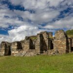 Estructuras de piedra del sector Hanan en Choquequirao sobre una colina verde, bajo un cielo dramático y con vistas al cañón andino.