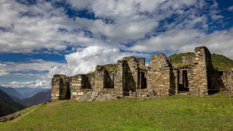 Estructuras de piedra del sector Hanan en Choquequirao sobre una colina verde, bajo un cielo dramático y con vistas al cañón andino.