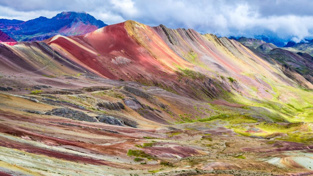 Laderas de la Montaña Vinicunca revelando sus vibrantes franjas de colores minerales bajo un cielo dramático en Cusco.