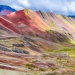 Laderas de la Montaña Vinicunca revelando sus vibrantes franjas de colores minerales bajo un cielo dramático en Cusco.