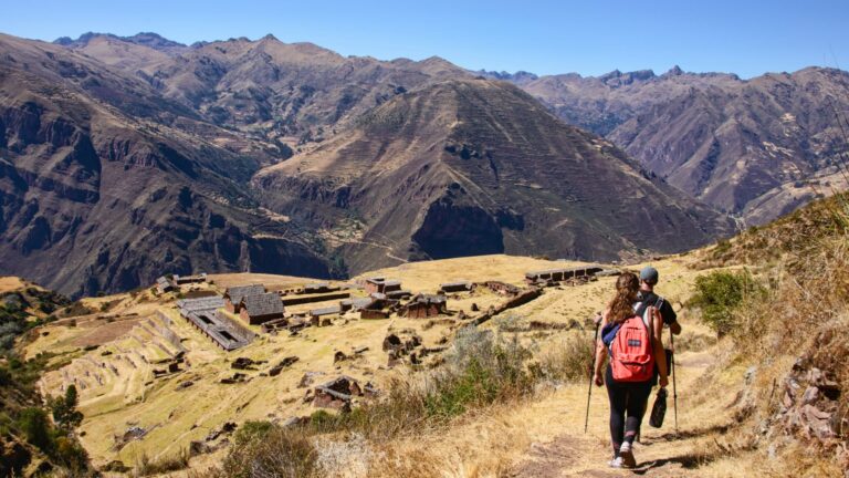 Dos excursionistas caminando por un sendero andino con vistas a las antiguas ruinas incas de Huchuy Qosqo en el Valle Sagrado.