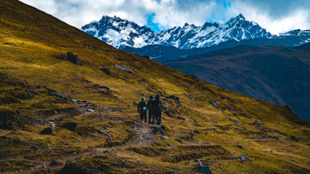 Tres montañistas ascienden por una ladera dorada hacia las imponentes cumbres de Lares Trek de la cordillera de los Andes en Perú.