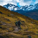 Tres montañistas ascienden por una ladera dorada hacia las imponentes cumbres de Lares Trek de la cordillera de los Andes en Perú.