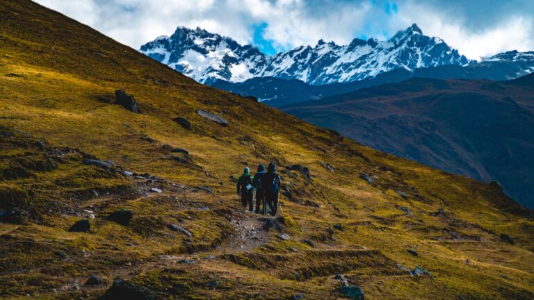 Tres montañistas ascienden por una ladera dorada hacia las imponentes cumbres de Lares Trek de la cordillera de los Andes en Perú.