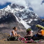 Viajera conversando con dos artesanas andinas que muestran sus textiles tradicionales a los pies del Nevado Ausangate en Perú.
