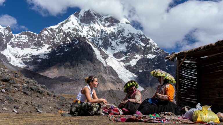 Viajera conversando con dos artesanas andinas que muestran sus textiles tradicionales a los pies del Nevado Ausangate en Perú.