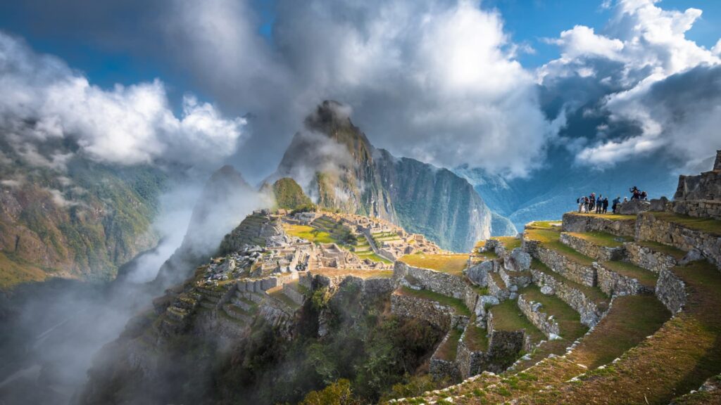 La icónica ciudadela inca de Machu Picchu con la montaña Huayna Picchu de fondo, envuelta en nubes y niebla mística al amanecer.