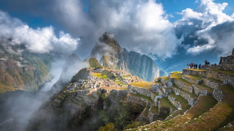 La icónica ciudadela inca de Machu Picchu con la montaña Huayna Picchu de fondo, envuelta en nubes y niebla mística al amanecer.