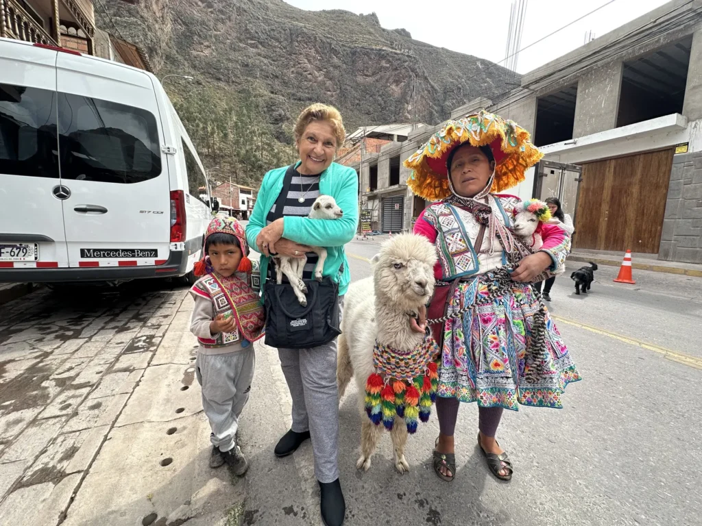 Viajera con una mujer en traje típico, un niño y una alpaca en una calle de Pisac
