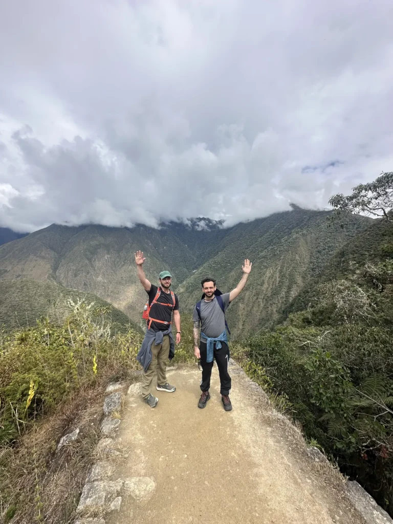 Dos caminantes celebrando con los brazos en alto en un sendero del Camino Inca con vista al valle