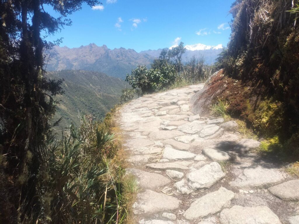 Sendero inca empedrado al borde de la montaña con nevados al fondo