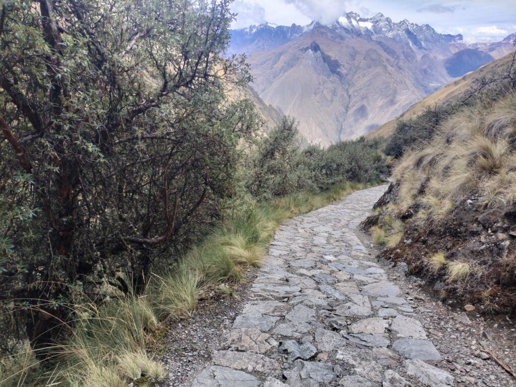 Sendero empedrado de subida al paso de Warmiwañusca con nevados detrás