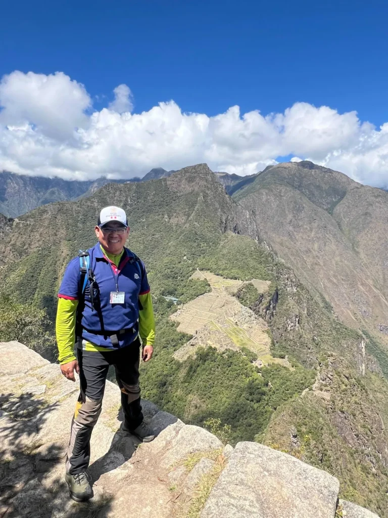 Deivis Pumalloclla, guía oficial de turismo, en la cumbre de Huayna Picchu con la ciudadela de Machu Picchu al fondo
