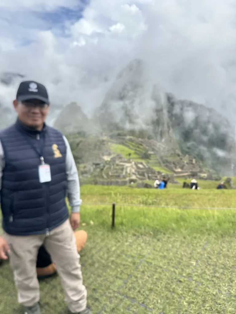 Deivis Pumalloclla con su carné de guía oficial de turismo en Machu Picchu, con la ciudadela entre nubes al fondo