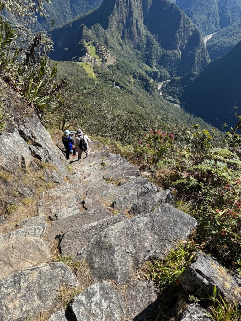 Caminantes en la escalinata empinada de la Montaña Machu Picchu, con la ciudadela abajo