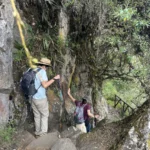 Caminantes subiendo una escalinata de piedra junto a una pared rocosa en el Camino Inca