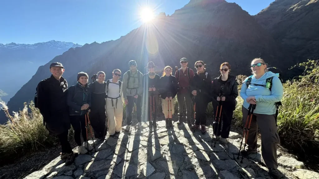 Grupo de viajeros con bastones en una escalinata inca del Camino Inca, a contraluz