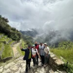 Grupo de viajeros en una escalinata inca del Camino Inca con montañas cubiertas de nubes