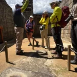 Guía oficial explicando a un grupo una roca tallada con cavidades de agua dentro de la ciudadela de Machu Picchu