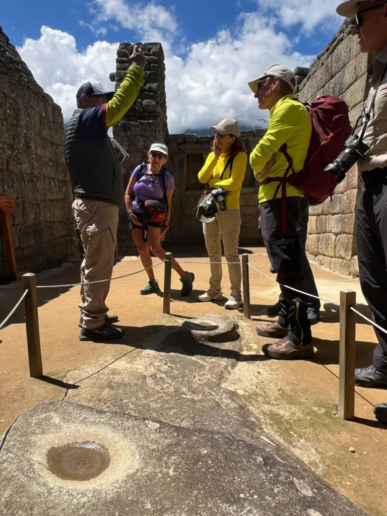 Guía oficial explicando a un grupo una roca tallada con cavidades de agua dentro de la ciudadela de Machu Picchu