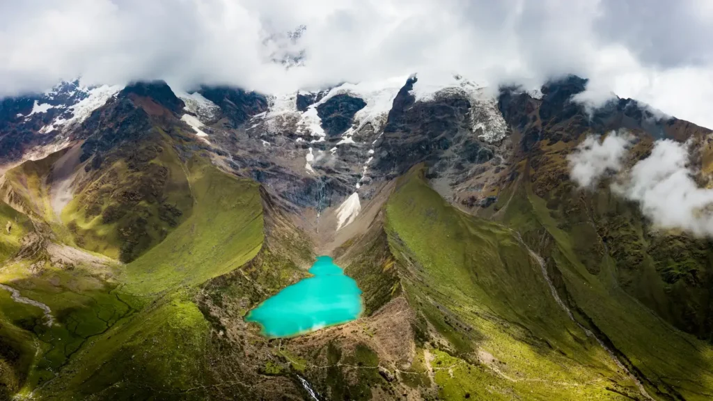 Vista aérea de la Laguna Humantay entre laderas verdes y el glaciar cubierto de nubes