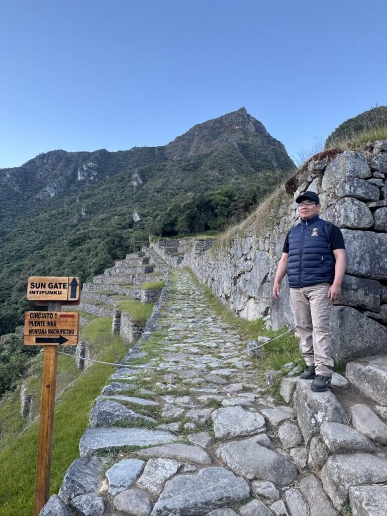 Deivis Pumalloclla, guía oficial, junto al letrero hacia el Intipunku y la Montaña Machu Picchu