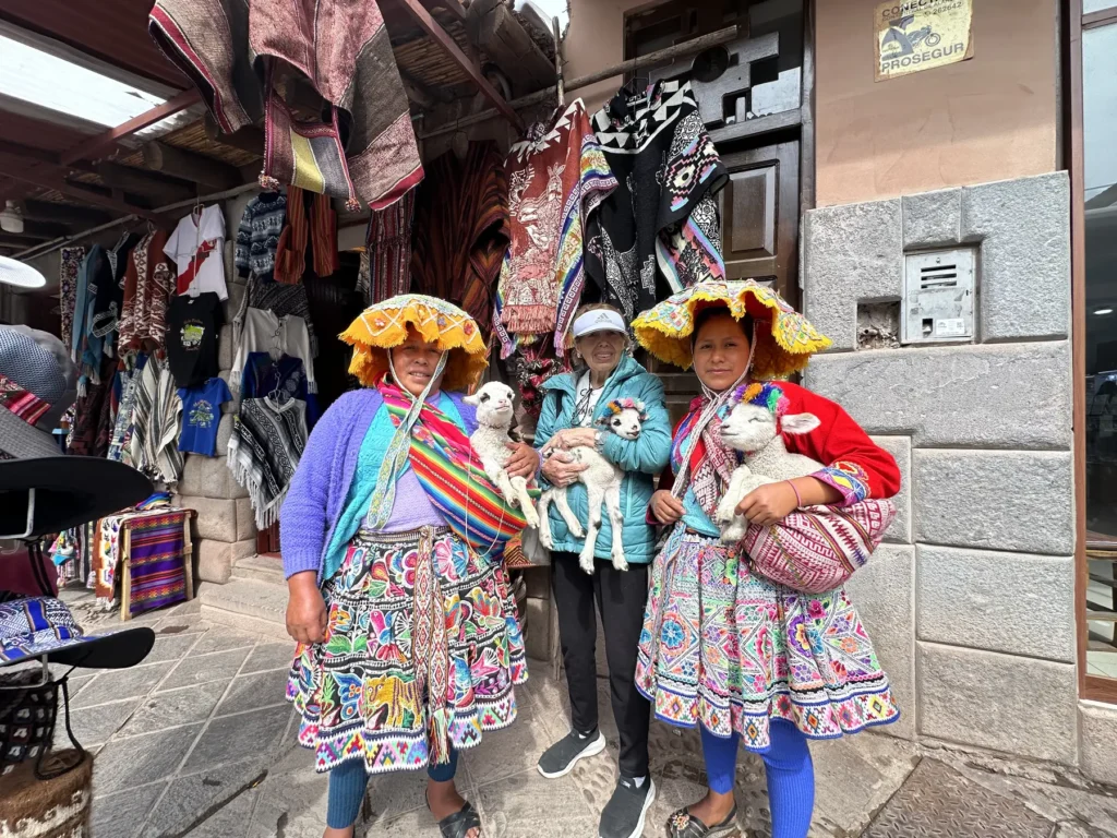 Viajera con mujeres en traje típico y corderos en una calle del mercado de Pisac