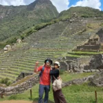 Pareja de viajeros frente a las terrazas agrícolas de Machu Picchu en un día soleado