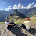 Viajeras sentadas frente a la ciudadela de Machu Picchu y Huayna Picchu en un día despejado