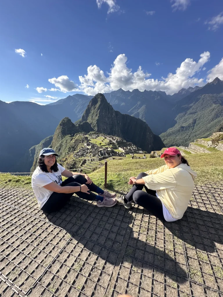 Viajeras sentadas frente a la ciudadela de Machu Picchu y Huayna Picchu en un día despejado