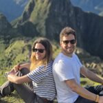 Pareja de viajeros sentados frente a Machu Picchu y el Huayna Picchu